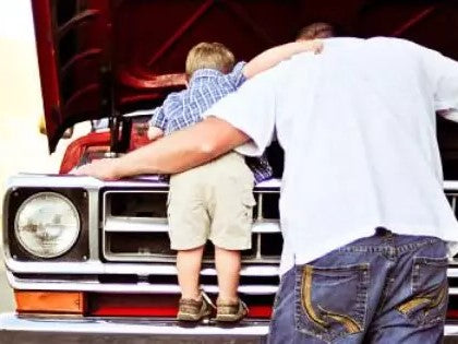 A dad and young child working on a classic pickup truck together