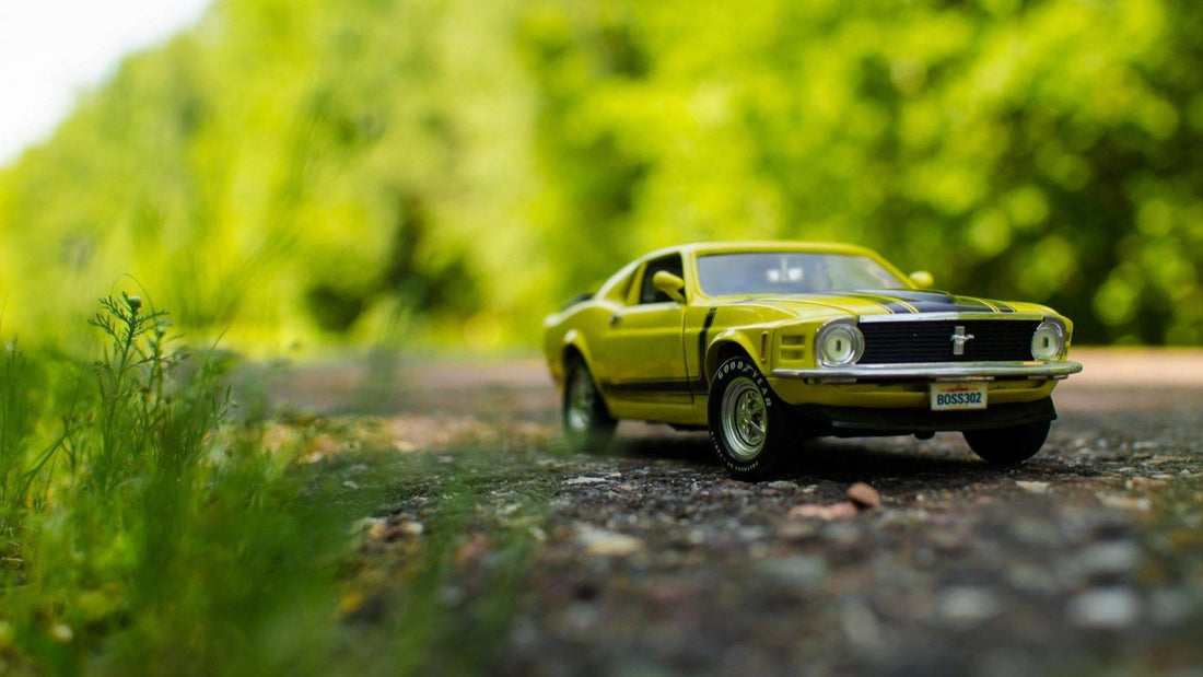 A diecast replica model of a lime green 1970s Ford Mustang GT with trees in the background